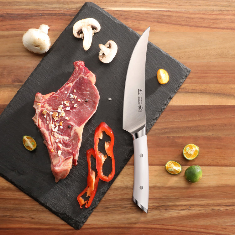 6-inch boning knife with white handle on black slate next to raw steak, mushroom slices, red pepper, and small citrus fruits.