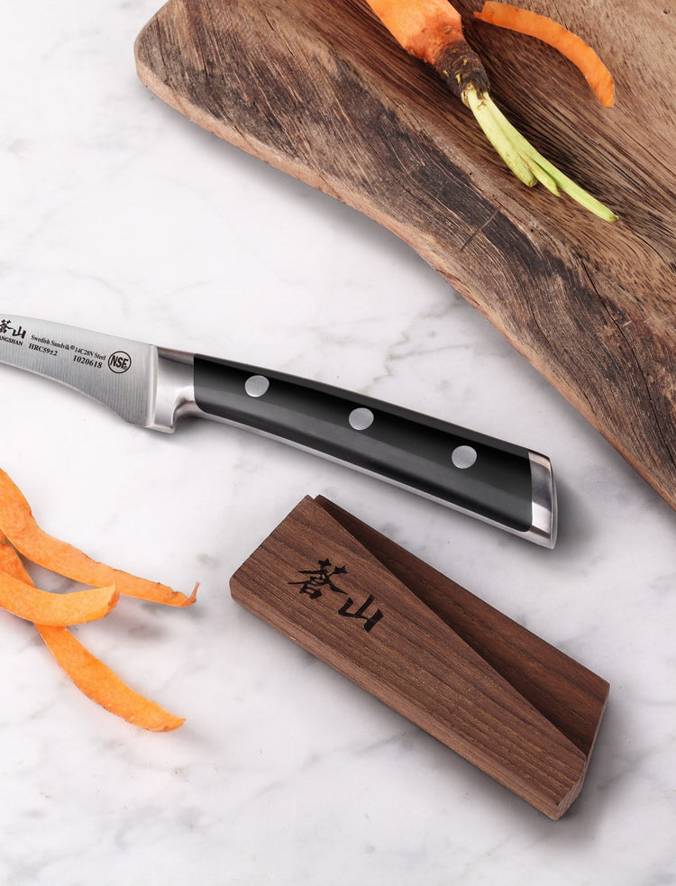 Black-handled chef’s knife beside an open dark wood magnetic sheath on a marble surface.