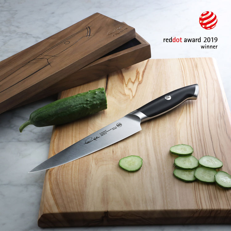 7-inch utility knife with black handle on wooden cutting board, partially sliced cucumber, wooden knife box nearby, Red Dot A