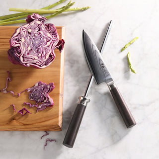 
                    
                      Crossed kitchen knife and honing steel with dark handles on marble surface next to chopped purple cabbage on wooden board.
                    
                  