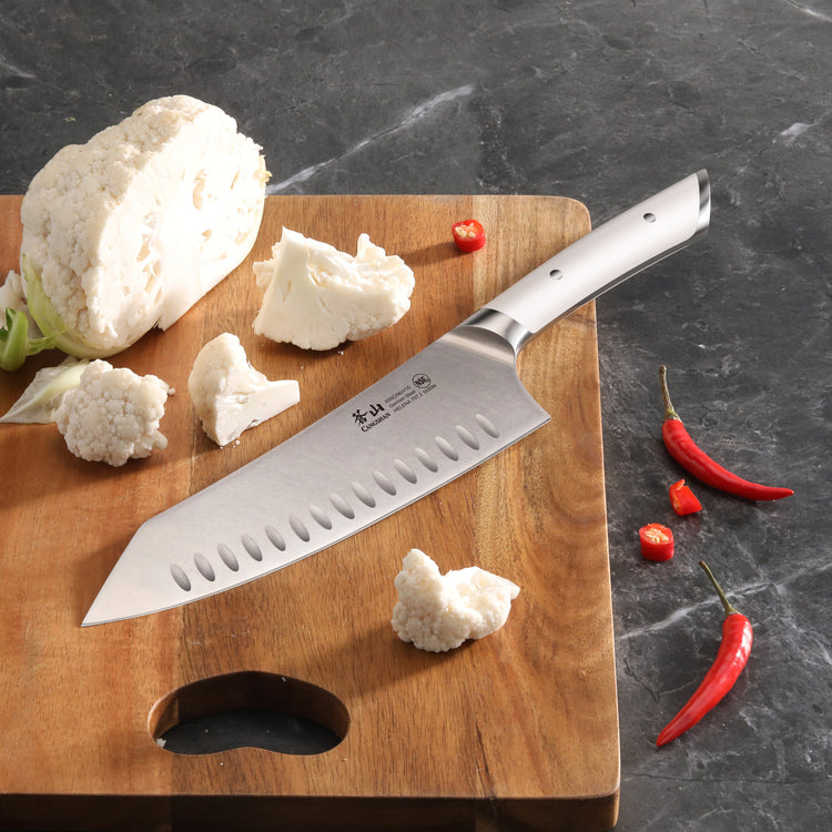 8-inch chef's knife with a white handle on a wooden cutting board with cauliflower and red chili peppers.