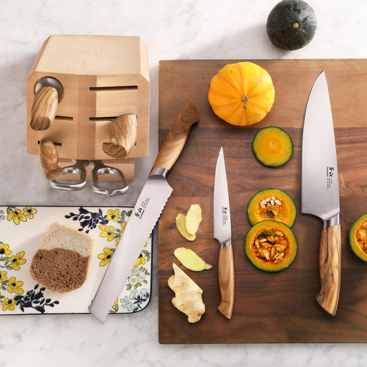 Wood-handled knives with a wooden block, sliced pumpkin, and ginger on a wooden cutting board.