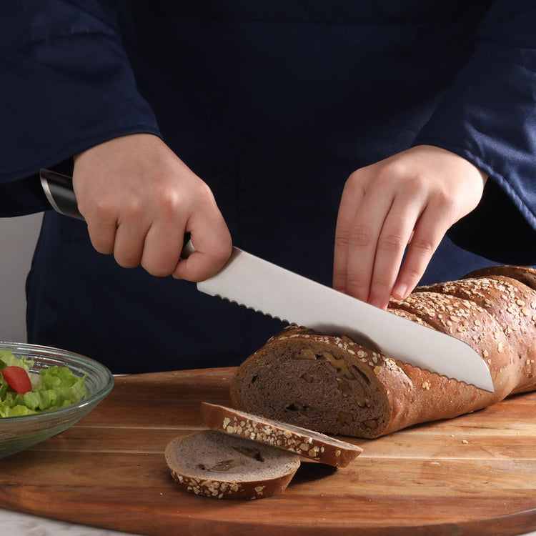 Person slicing a seeded loaf of bread on a wooden cutting board with a serrated bread knife.