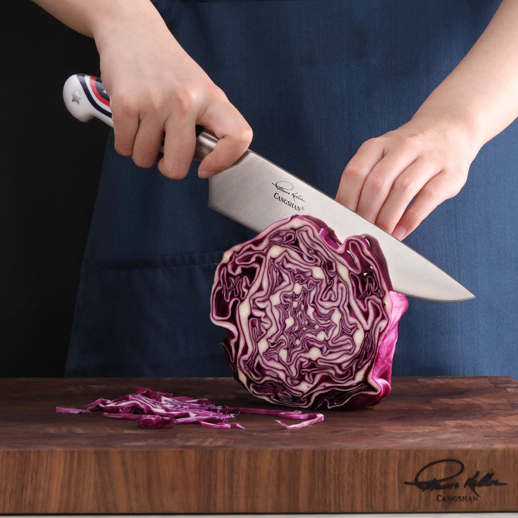 Person slicing a halved purple cabbage on a wooden cutting board with a chef's knife featuring an American flag design handle
