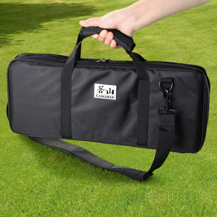 Black rectangular nylon knife bag with handles and shoulder strap, held by a hand against a grass background.