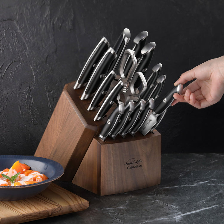 Hand pulling a knife from a wooden knife block set with black-handled knives and shears.