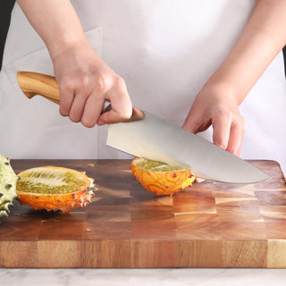 
                    
                      Person slicing a horned melon on a wooden cutting board with a large kitchen knife.
                    
                  