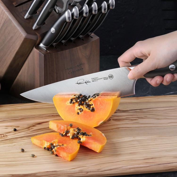 Hand slicing a papaya on a wooden cutting board with a chef's knife, beside a wooden knife block set.