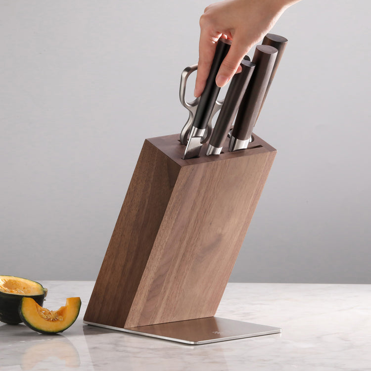 Hand removing a knife from a wooden knife block holding five knives with dark handles on a marble surface.
