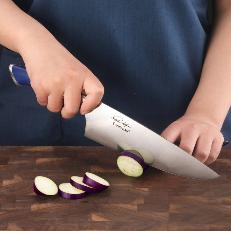 Person slicing a small eggplant with a blue-handled chef's knife on a wooden cutting board.