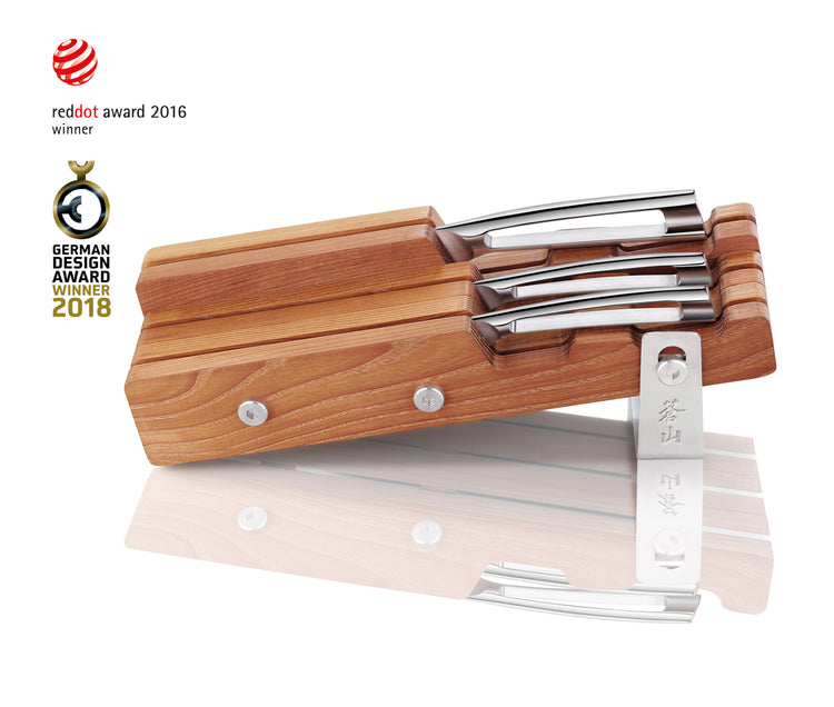Wooden knife block holding four stainless steel knives with one knife lying in front, showing award logos.